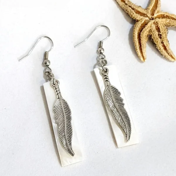 boucles d'oreilles en nacre et plumes posées à coté d'une étoile de mer